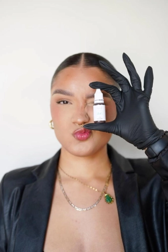 A young woman holding up a bottle of permanent makeup ink by her face - Aesthetically Speaking - Reno Nevada